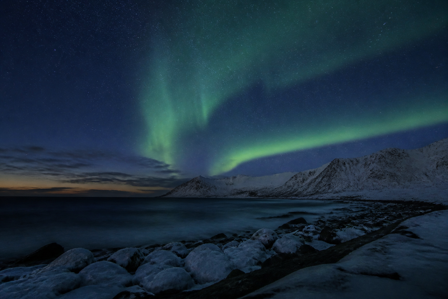 Northern Lights above a snowy Arctic coast and mountains